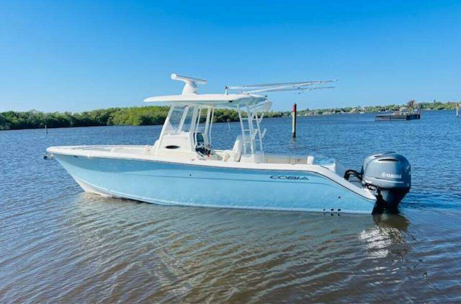 2021 Cobia 301 Center Console boat on calm water, clear blue sky background.